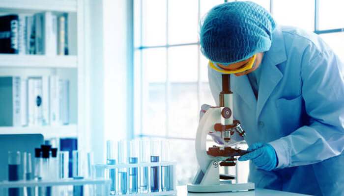 Research Laboratory researcher examining samples through a microscope to study biofilm structure and microbial growth.