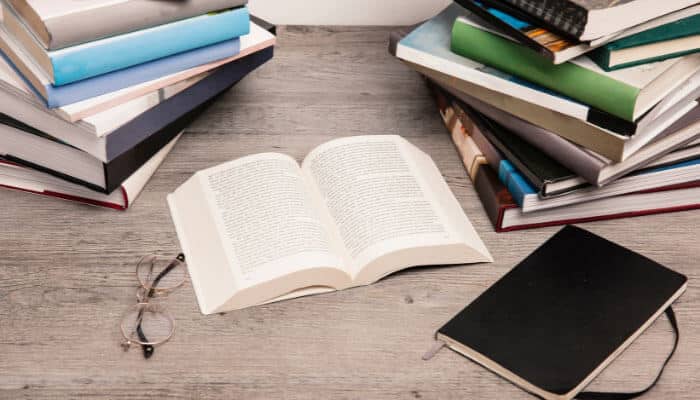 Education books on a social topic | tycoonstory media Open book surrounded by stacked books and glasses, emphasizing knowledge-sharing efforts of a social enterprise.