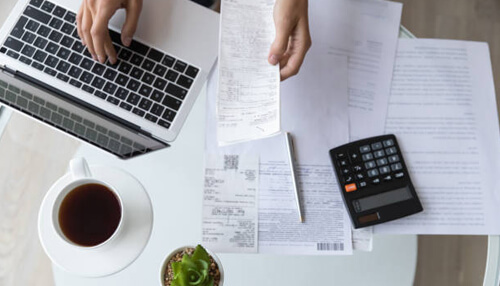 Bookkeeping - tycoonstory | tycoonstory media Starting a business: organizing documents and working on a laptop to plan business finances.