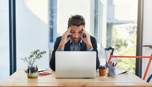 Tips for new entrepreneurs Man sitting at a desk in front of a laptop, holding his head in frustration, symbolizing stress or overwhelm in the workplace.