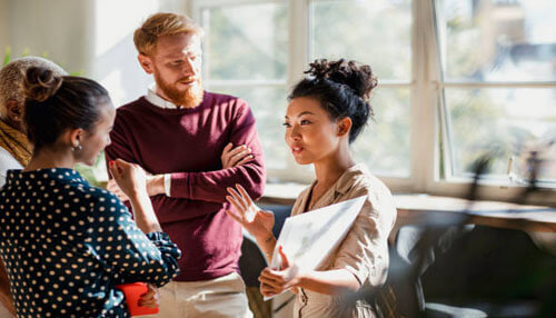 Brainstorming A group of professionals engaged in a discussion in a bright office space, with one woman presenting and sharing ideas.
