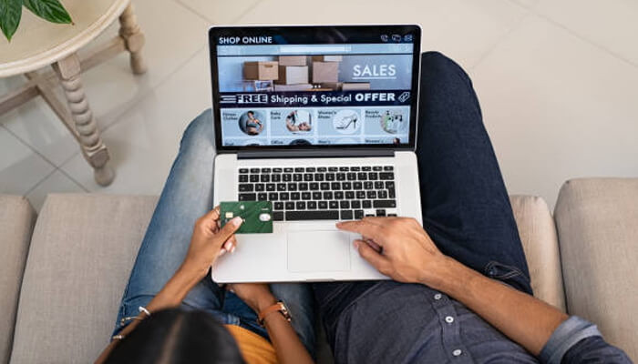 Ecommerce website Person sitting on a couch using a laptop to shop online while holding a credit card, browsing products and offers on an ecommerce website, illustrating online purchasing and digital retail.