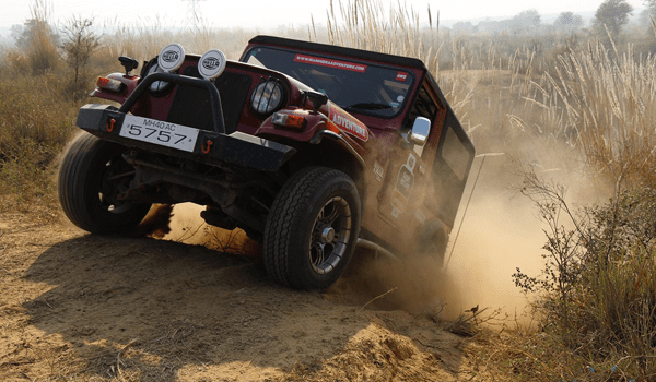 Mahindra thar A rugged mahindra off-road jeep climbing a steep dirt trail, throwing dust as it powers through uneven terrain.