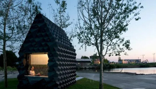 Urbаn cаbin - tycoonstory | tycoonstory media Small geometric cabin built using advanced 3d printing methods beside a lakeside, representing modern 3d printed houses design.