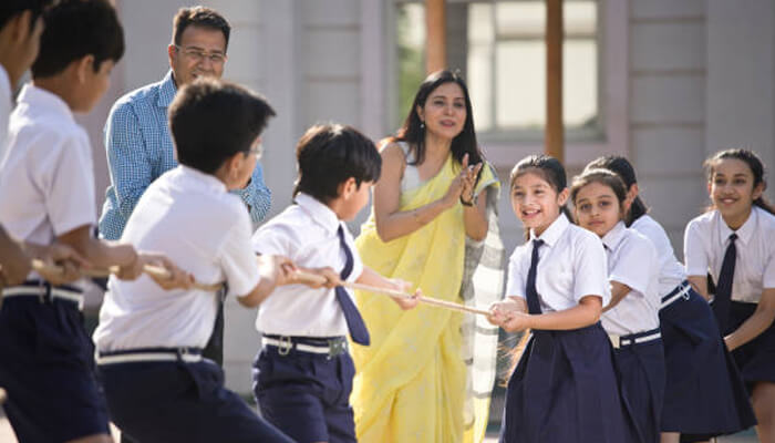 Championship School children enthusiastically playing tug of war during a school-level championship, cheered on by teachers and classmates outdoors.