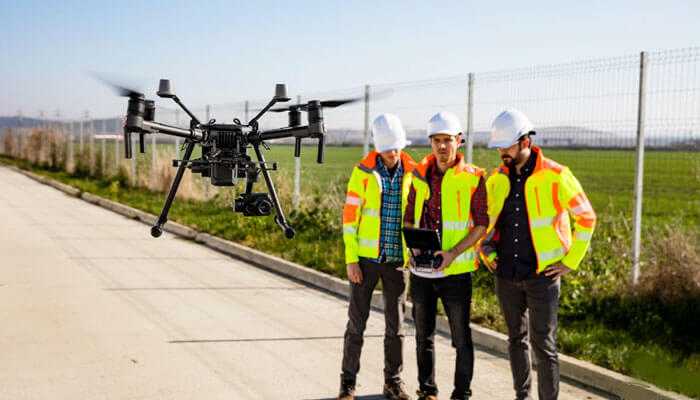 Draft regulations to uav's A group of construction workers in safety gear standing on a road, while a drone flies overhead, showcasing the use of uavs (unmanned aerial vehicles) in industry, with implications for draft regulations to uavs.
