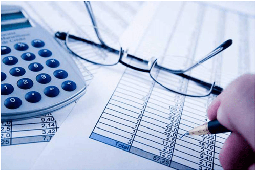 Tax reporting document- tycoonstory | tycoonstory media Close-up of financial statements with calculator, glasses, and a hand writing numbers on a spreadsheet.