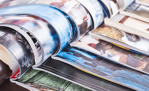 Writing for magazines Close-up of several open magazines with glossy colorful pages spread out in layers.