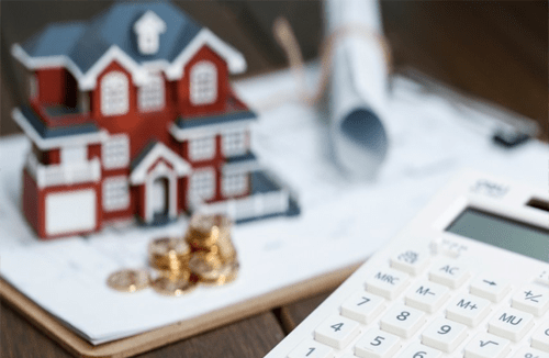Second mortgage house loan -tycoonstory | tycoonstory media Model house, coins, and calculator on desk representing mortgages, home loans, and financial planning.