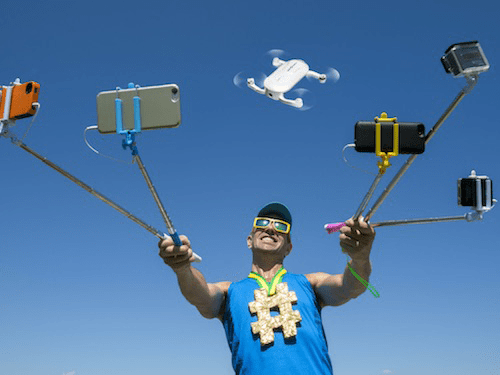 Alternative start-up ideas Man posing with multiple selfie sticks and smartphones attached while a drone flies overhead.