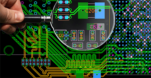 Designing and printing the pcb A hand holding a magnifying glass over a complex, multicolored design layout for printed circuit boards, showing traces and components.