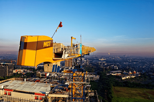 Terrain mobile cranes Large yellow tower crane overlooking a cityscape during sunrise, positioned above buildings and construction sites.