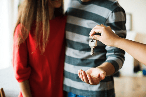 Mortgage A person handing over a key to a couple, symbolizing home ownership and the role of income in securing a mortgage.