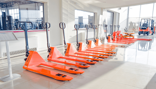 Forklifts - tycoonstory | tycoonstory media Orange pallet jacks lined up in a showroom used in the material handling industry.