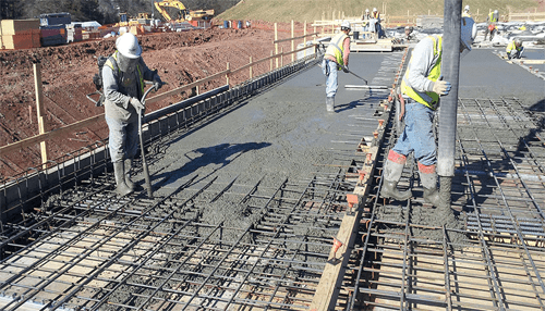 Civil engineering Construction workers pouring and leveling concrete over reinforced steel framework, showcasing civil engineering services provided by an engineering firm for large-scale infrastructure projects.