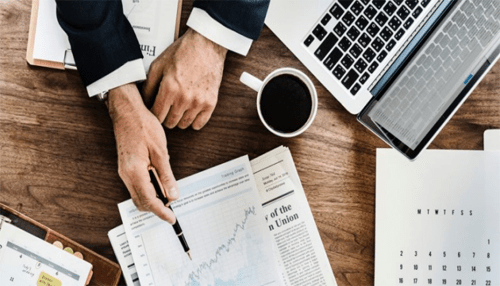 Educate yourself - tycoonstory | tycoonstory media Person analyzing financial reports and charts, with a cup of coffee and a laptop on the desk, symbolizing business analysis and decision-making.