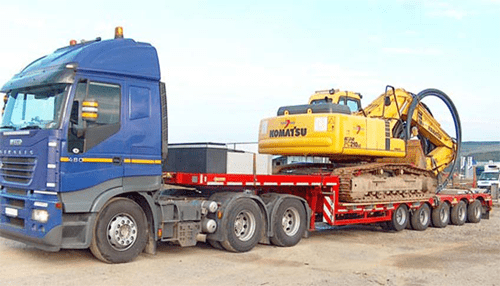 Machinery relocation - tycoonstory | tycoonstory media A large truck hauling a komatsu excavator on a flatbed trailer, showcasing heavy equipment transportation for machinery relocation services.