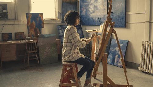 Artist painting on an easel in a studio with several completed artworks on display, highlighting the importance of reproduction prints for sharing art with a wider audience.