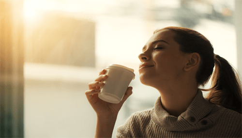 Starbucks A woman enjoying a cup of coffee, with a serene expression, as sunlight filters through a window in the background.