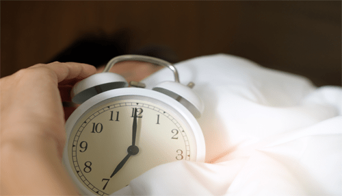 A guide to the perfect morning ritual A hand reaching to turn off an alarm clock, symbolizing the beginning of a productive and intentional morning ritual.