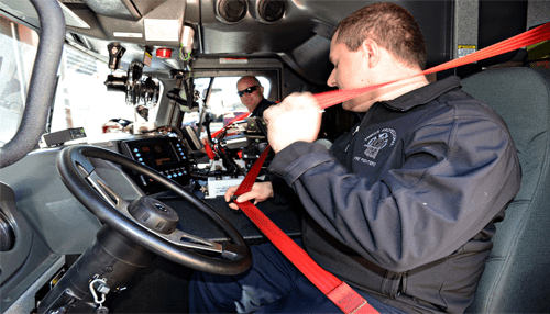 Wear your seatbelt - tycoonstory | tycoonstory media Truck driver fastening a bright red seatbelt inside a truck cab while another driver sits in the background, illustrating essential safety tips for truck drivers.