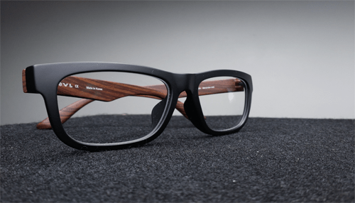 Warby parker ecommerce site A pair of black-framed eyeglasses with wooden temples placed on a textured dark surface.