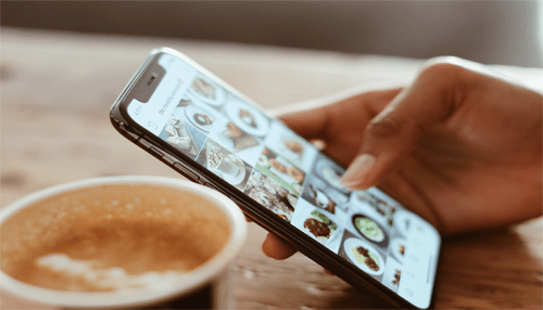 Food business Food business social media promotion concept showing a person browsing food photos on a smartphone next to a cup of coffee in a café setting.