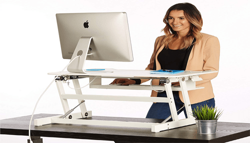 Weight loss - tycoonstory | tycoonstory media Smiling professional using a standing desk riser to create a healthier workspace environment.