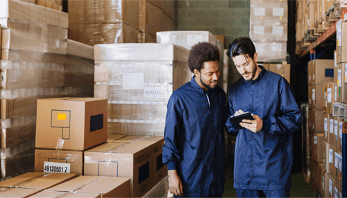 The image shows two workers in a warehouse, surrounded by boxes and packages, reviewing information on a clipboard. This scene represents dropshipping business Warehouse staff checking inventory and shipments in a fulfillment center, representing order processing in dropshipping