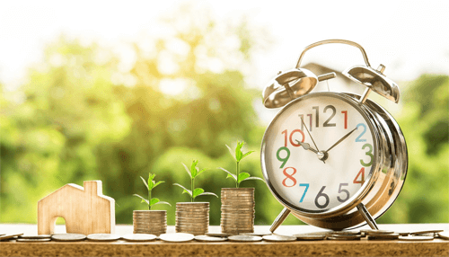 Personal finances Growing coin stacks with young plants beside a clock and house model, representing long-term savings, investments, and planning for strong personal finances.