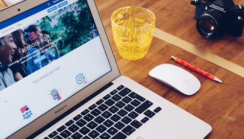 Cost-effective marketing A laptop opened to facebook ads with a mouse and camera on the desk, showcasing digital marketing and social media advertising.