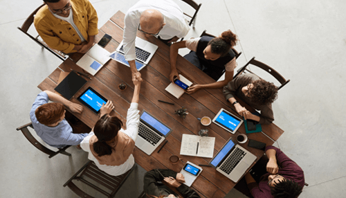 "group of professionals meeting around a wooden table, shaking hands and collaborating with laptops and tablets present, symbolizing business networking and partnership The role of business networking in understanding the business environment