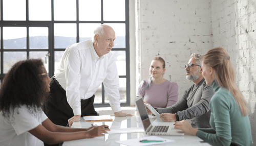 Looker Business team in a meeting with an older leader standing at the table, discussing strategies enhanced by business intelligence tools.