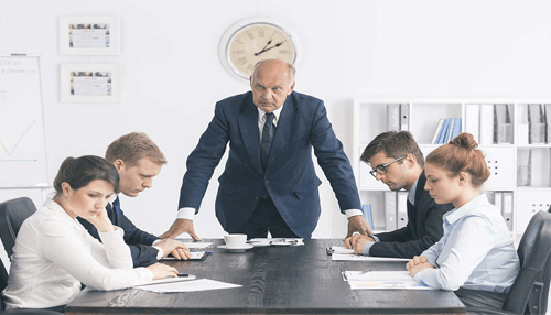 Criticism at workplace-tycoonstory | tycoonstory media A group of business professionals in a tense meeting, with the senior manager standing while the others sit, representing the importance of honesty in addressing workplace challenges.