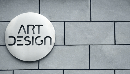 Modern circular sign displaying'ART DESIGN' on a textured gray wall, emphasizing a sleek and contemporary aesthetic Minimalist art and design wall sign representing creative branding and professional office aesthetics.