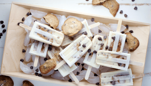 Delicious ice pops with chocolate chips on ice, accompanied by chocolate chip cookies in a rustic wooden tray Assorted dessert treats including cookies and ice pops arranged on a tray, suitable for office celebrations.