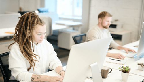 How many hours a week - tycoonstory | tycoonstory media Two people working in a modern office space, focused on their tasks at computer desks, illustrating a productive work environment.