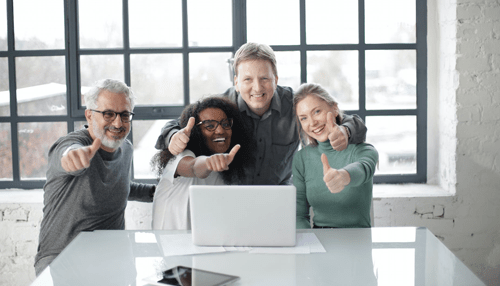 Technology reduce workplace stress Group of happy coworkers giving thumbs up while gathered around a laptop, showing teamwork and workplace positivity.