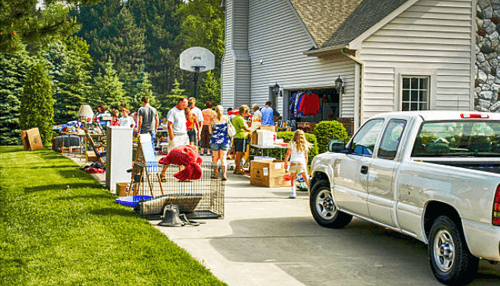 Estate sales-tycoonstory | tycoonstory media People browsing an outdoor estate sales on a sunny driveway with tables of goods and a white pickup truck.
