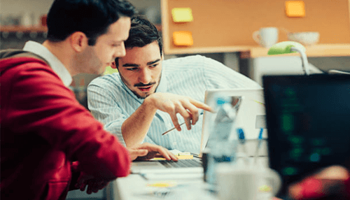 Incubator and accelerator Two men collaborate on a computer in an office, discussing incubators vs accelerators.