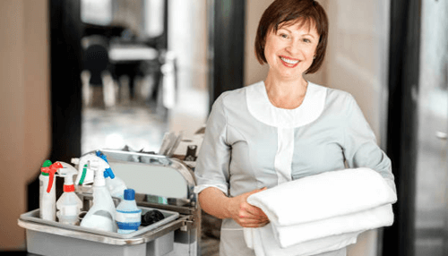 Housekeeping duties -tycoonstory | tycoonstory media Smiling caregiver holding fresh towels and cleaning supplies while providing home care assistance with housekeeping duties.