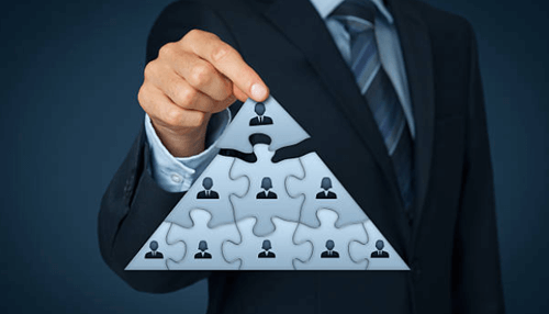 Mlm marketing strategy-tycoonstory | tycoonstory media A professional in a suit holding a triangular puzzle, symbolizing the structure and relationships within a multi-level marketing (mlm) system