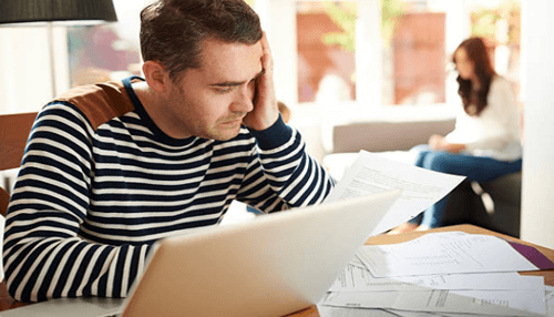 Tax stress-tycoonstory | tycoonstory media A man engaged with paperwork and a laptop at a table, assessing red flags in his tasks.