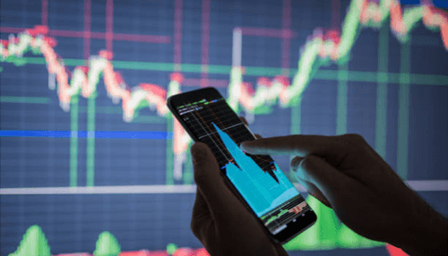 Mobile trading for brokering -tycoonstory | tycoonstory media Person analyzing stock market trends on a mobile phone, with a large graph of financial data displayed in the background.