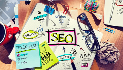 Off-page seo external optimization process - tycoonstory | tycoonstory media Flat lay of a workspace with a notebook filled with seo-related diagrams, including keywords, research, and content strategies, along with a cup of coffee and glasses.