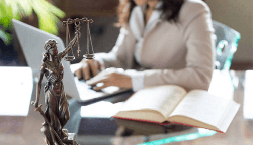 Sexual harassment lawyers near me - tycoonstory | tycoonstory media Legal workplace setting with a justice statue, law books, and a professional woman working, symbolizing laws and awareness against sexual harassment.