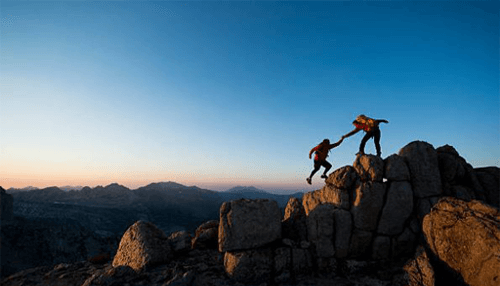 Strong relationship with your boss-tycoonstory | tycoonstory media Two climbers helping each other on a rocky mountain, representing teamwork and support in overcoming challenges.