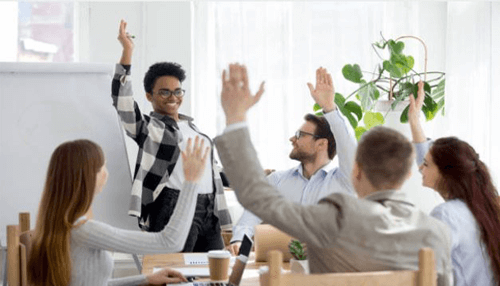 Volunteer for your team-tycoonstory | tycoonstory media A group of people at a meeting with one person raising their hand, symbolizing participation, leadership, and visibility in a group setting.