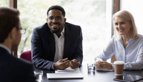 Final expense insurance age eligibility-tycoonstory | tycoonstory media A diverse group of professionals discussing final expense insurance options in a meeting room, with a man smiling and engaging in conversation.