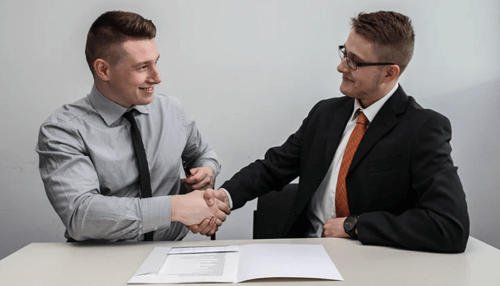 Potential business buyers -tycoonstory | tycoonstory media Two professionals shaking hands over a business contract, marking the agreement to sell your business.